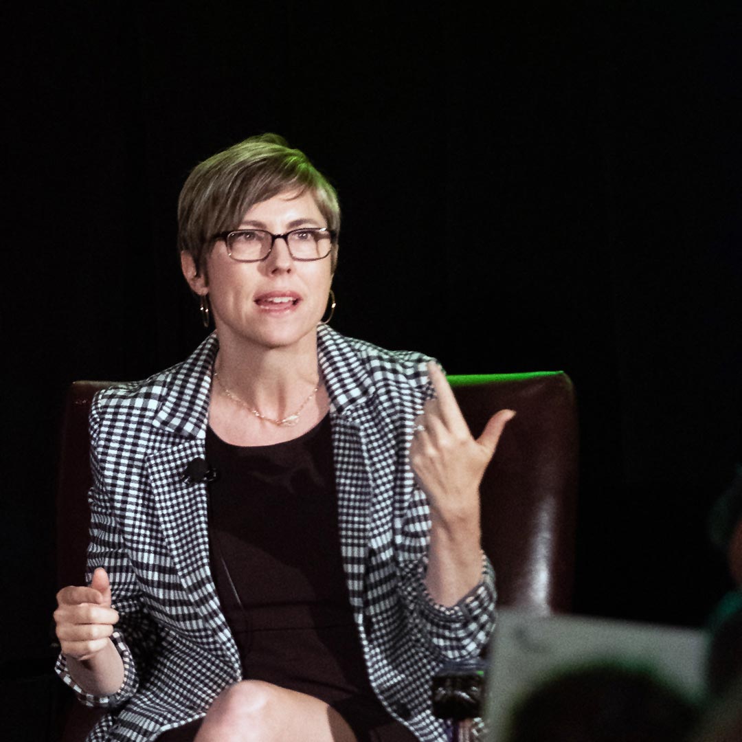 Monica Landers speaks seated in a leather chair on a dark background